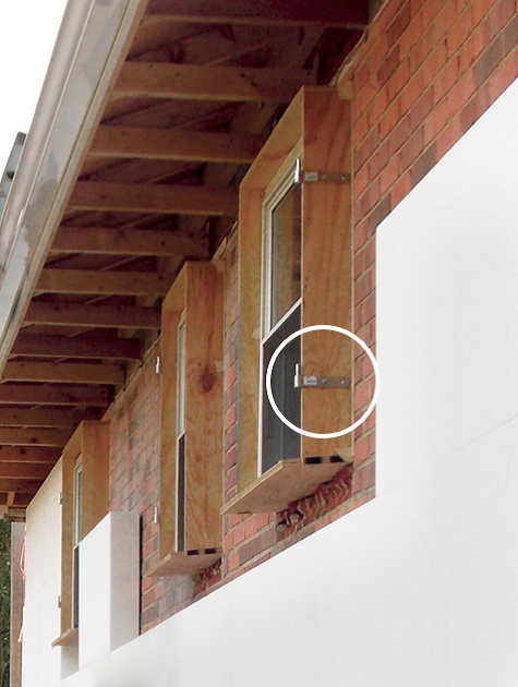 Close-up of a building exterior showing brick wall with three small wooden boxes attached to the wall around a window, under an unfinished wooden roof structure.