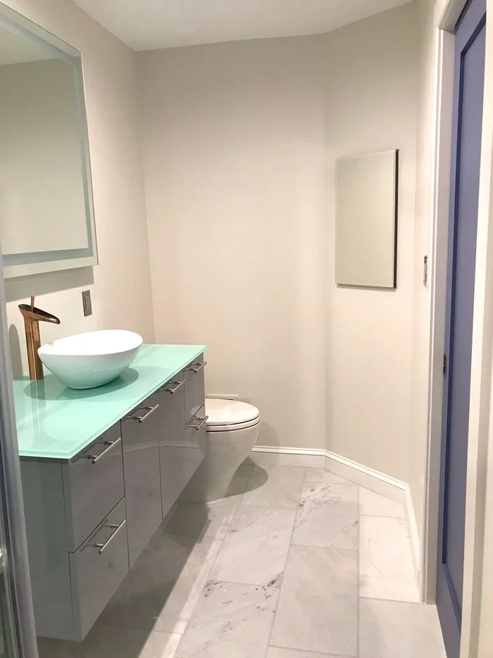 Modern bathroom with white walls, marble floors, a floating vanity with a vessel sink, a bronze faucet, and a toilet.