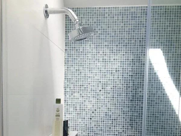 Showerhead attached to a tiled bathroom wall with small blue and white mosaic tiles.