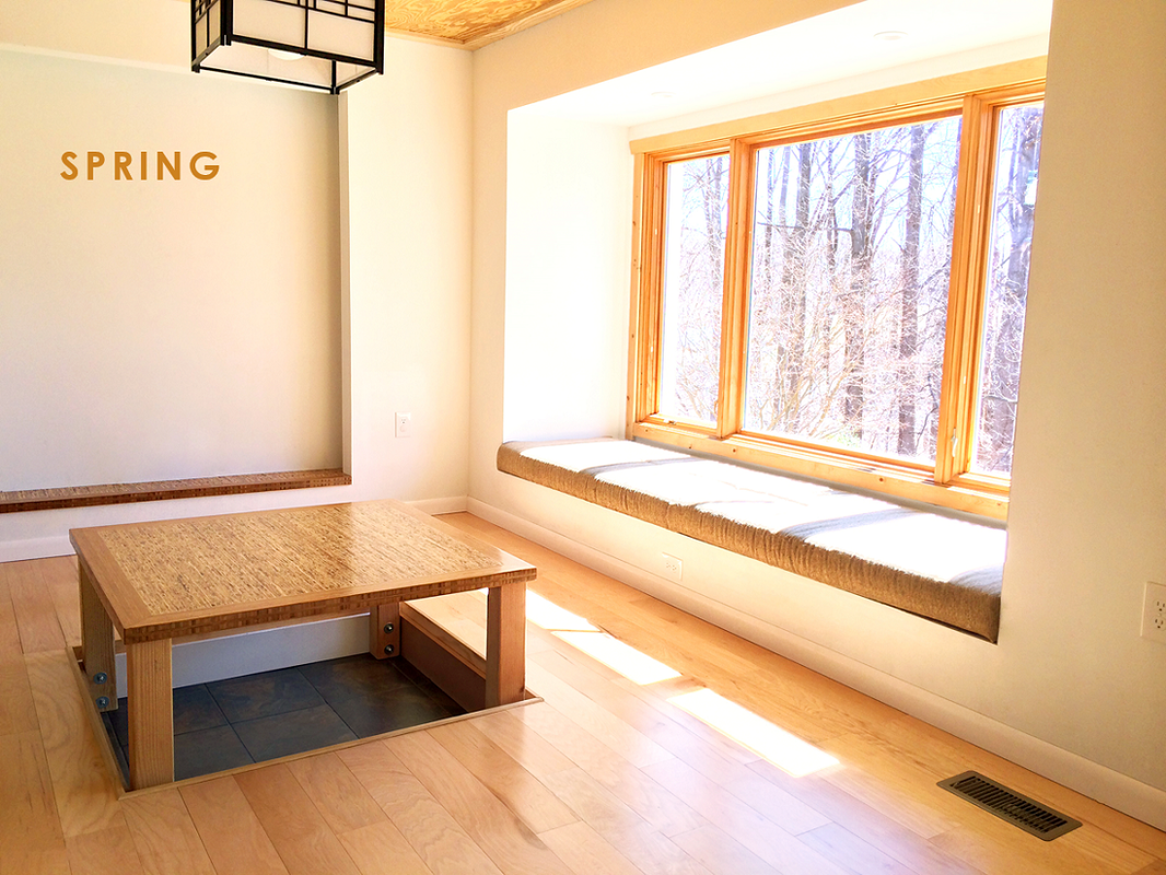 Bright room with large window seat, wooden window frames, and a low wooden table on a light hardwood floor.