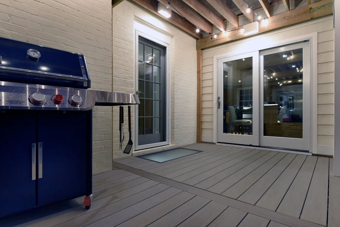 An enclosed outdoor patio area with a stainless steel gas grill, a door with glass panes, a sliding glass door, and string lights on the ceiling.