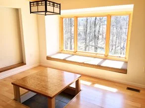 Room with large window seat overlooking snowy trees, with a wooden coffee table in the center.