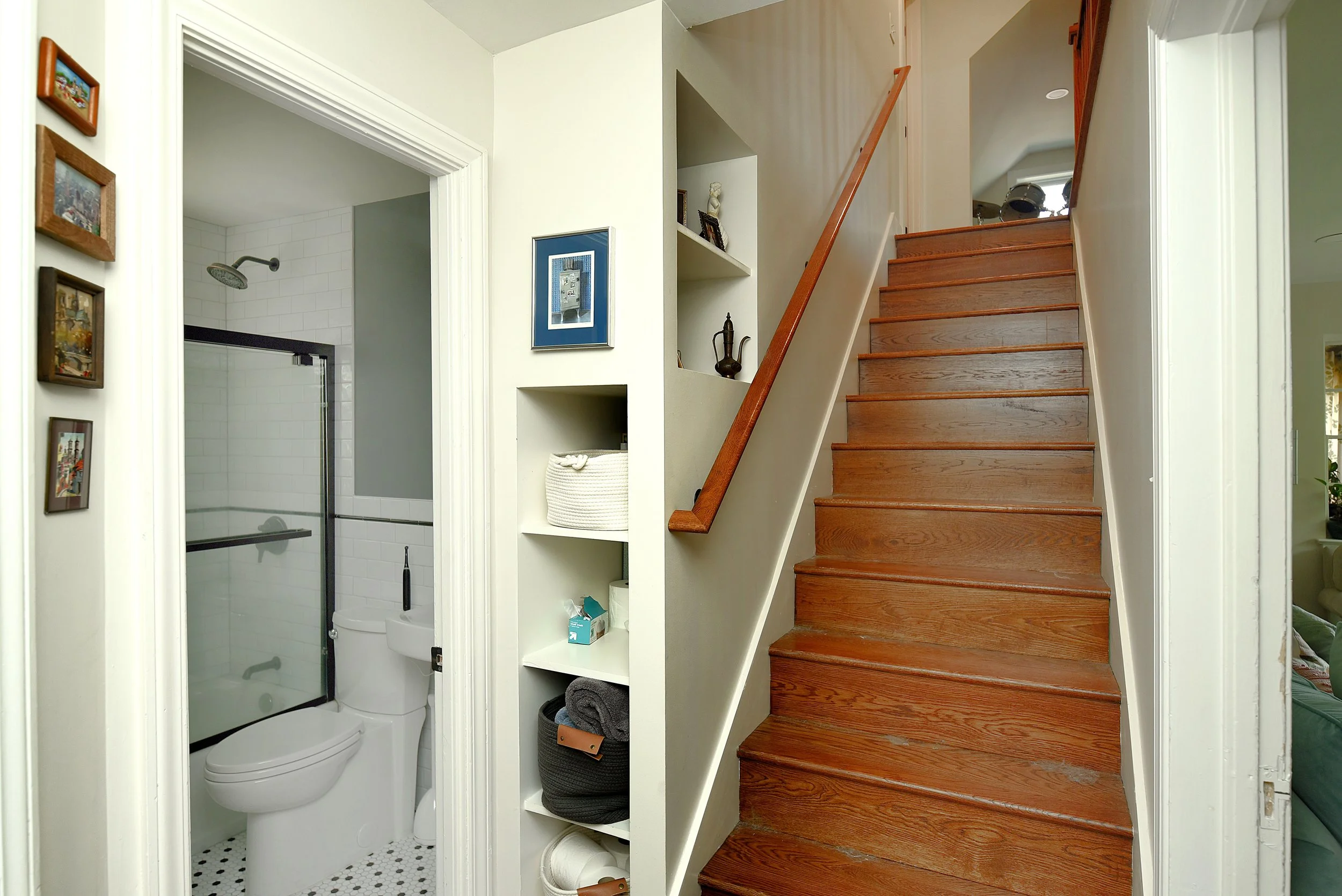 Interior view of a home showing a staircase with wooden steps, a small built-in shelf with decorative items and books, and an adjacent bathroom with a shower and toilet.