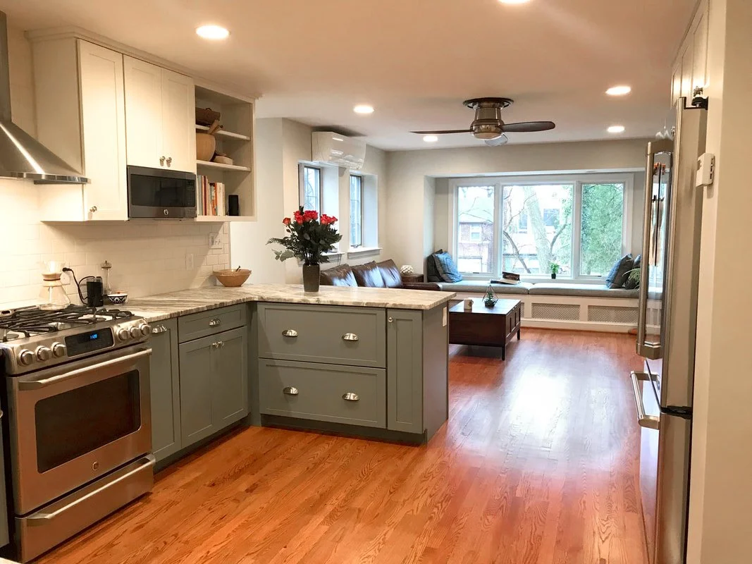 Open-concept kitchen and living room with hardwood floors, white cabinets, stainless steel appliances, a microwave, and a large window seat with cushions.