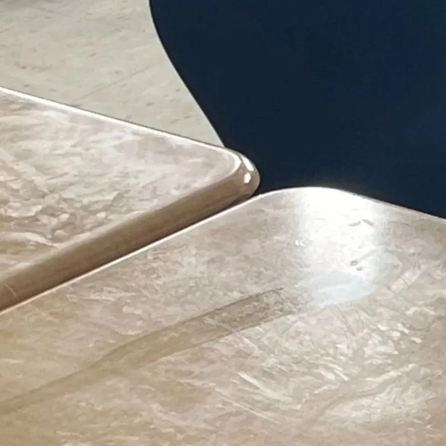 Close-up of two beige marble or stone tabletops with rounded edges, one partially overlapping the other.