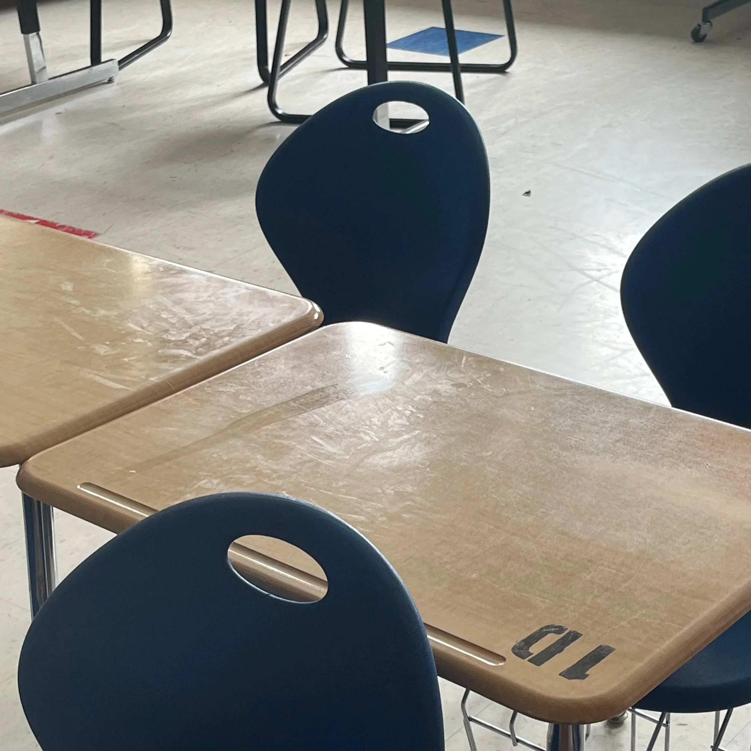 Empty classroom with wooden desks and dark blue chairs, one desk has the label 'TOP' on it.