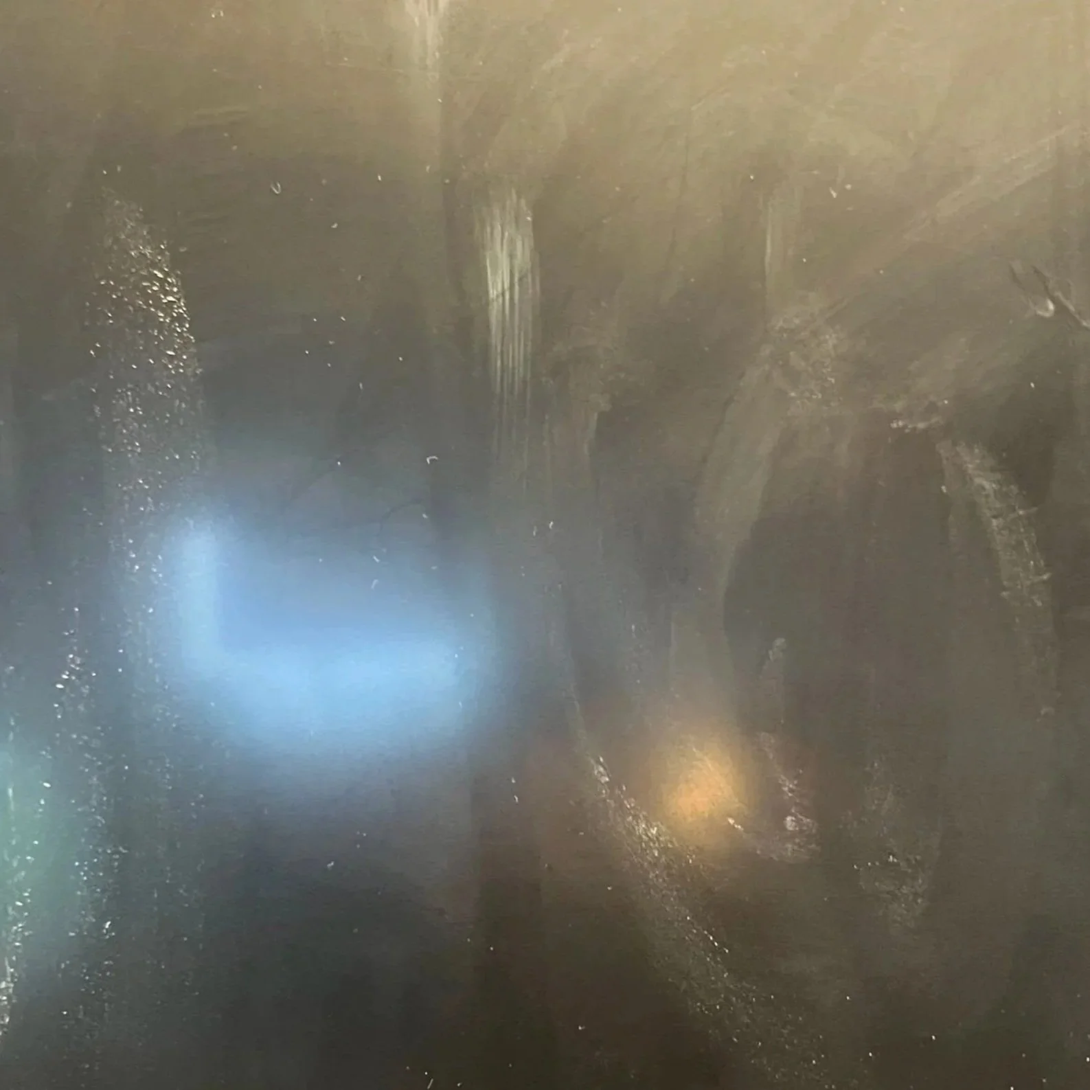 A foggy, dark surface with reflections of light, possibly an old mirror or glass pane.