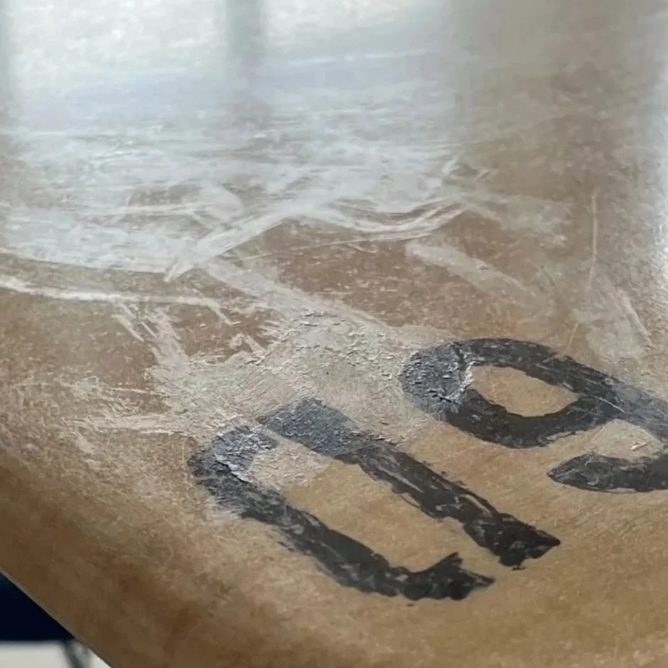 Close-up of worn black-painted letters on a brown cardboard surface.