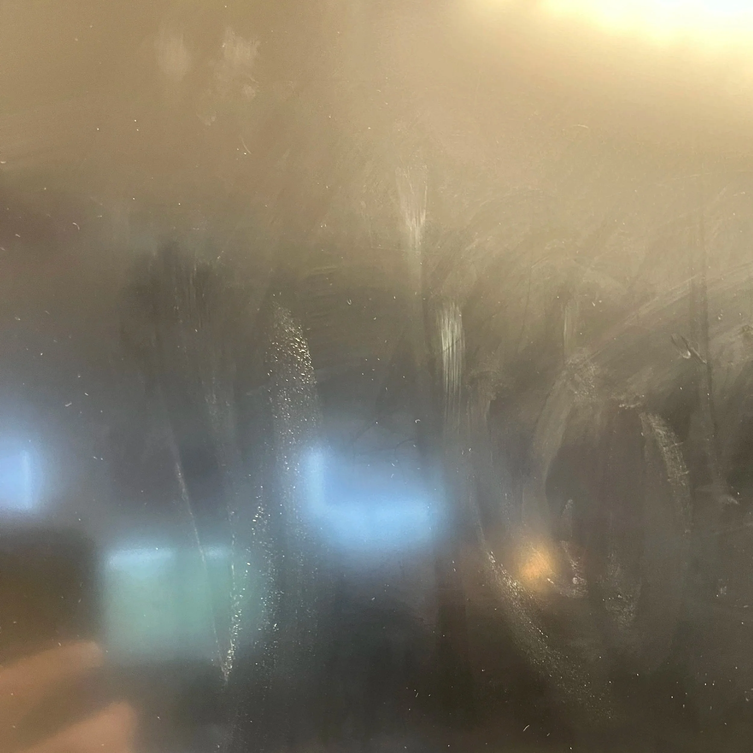 A dirty, foggy glass surface with streaks and smudges, and blurry lights in the background.