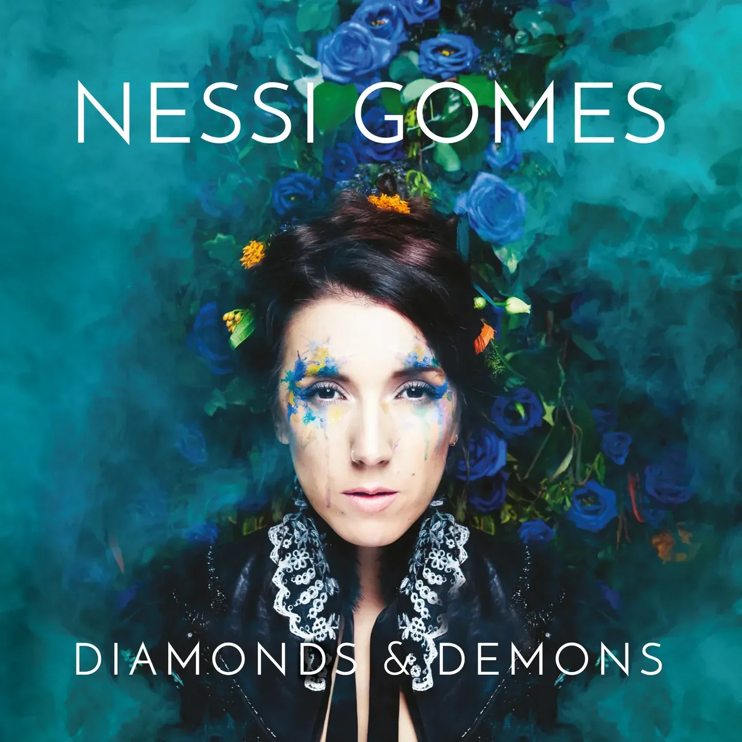 Album cover featuring a woman with dark hair and colorful face paint, lying amidst blue roses, with the text "Nessi Gomes Diamonds & Demons" at the top and bottom.