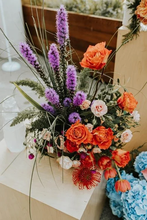 A colorful floral arrangement with purple, orange, pink, and red flowers on a light-colored surface.