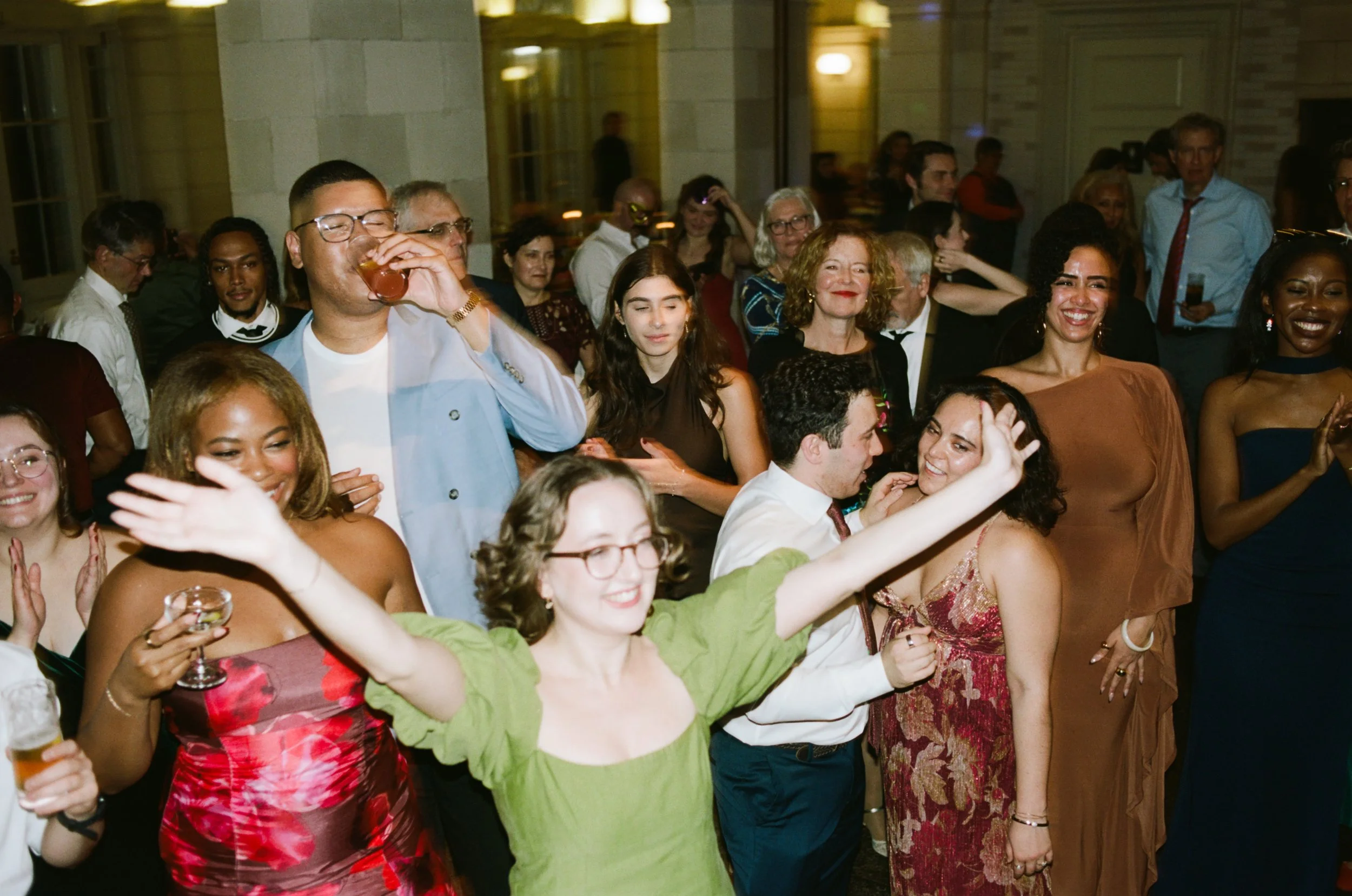 People dancing and celebrating at an indoor party, with some holding drinks and smiling.