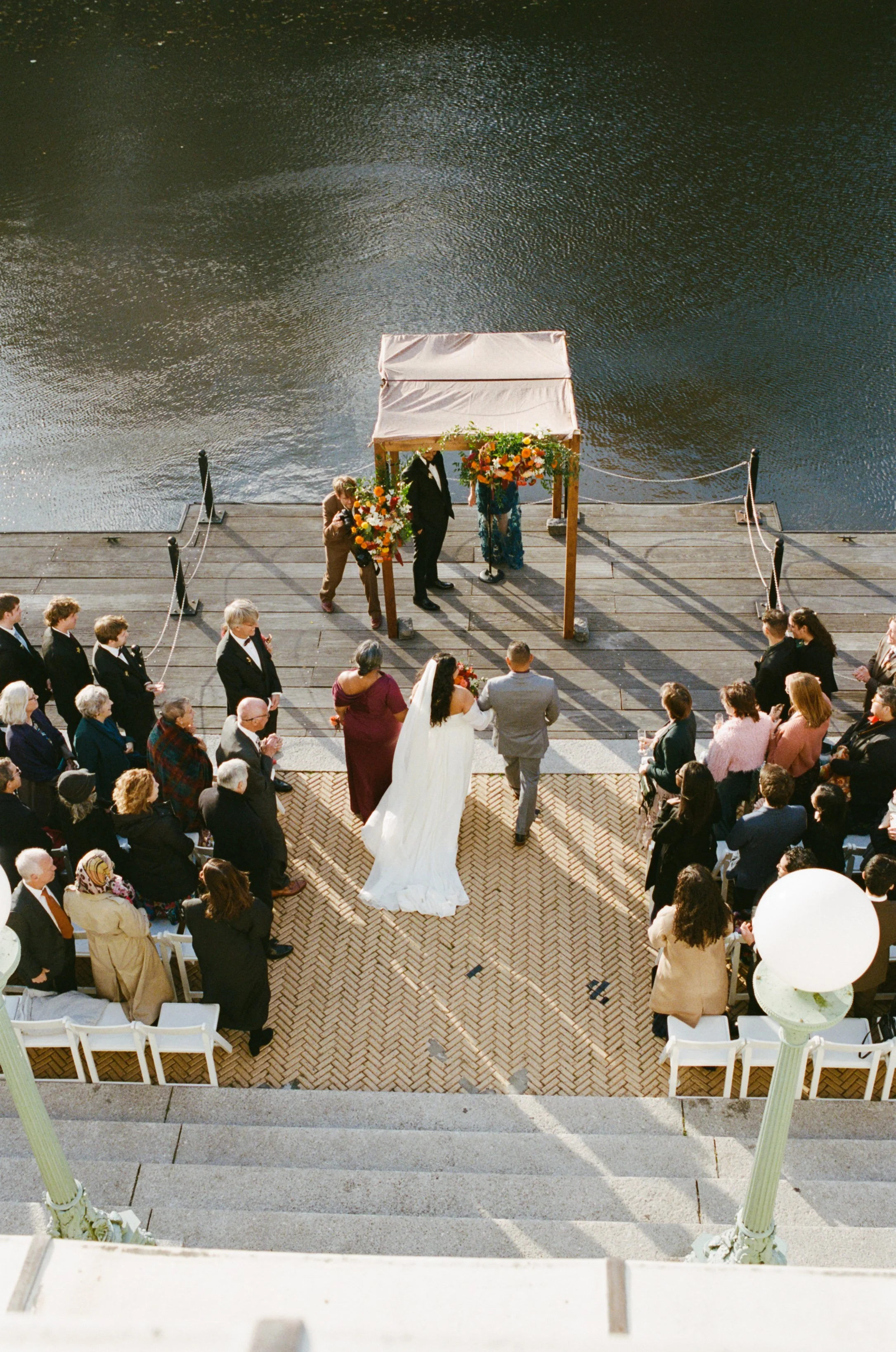 An outdoor wedding ceremony on a dock by a body of water, with guests seated and a bride and groom standing at the altar.