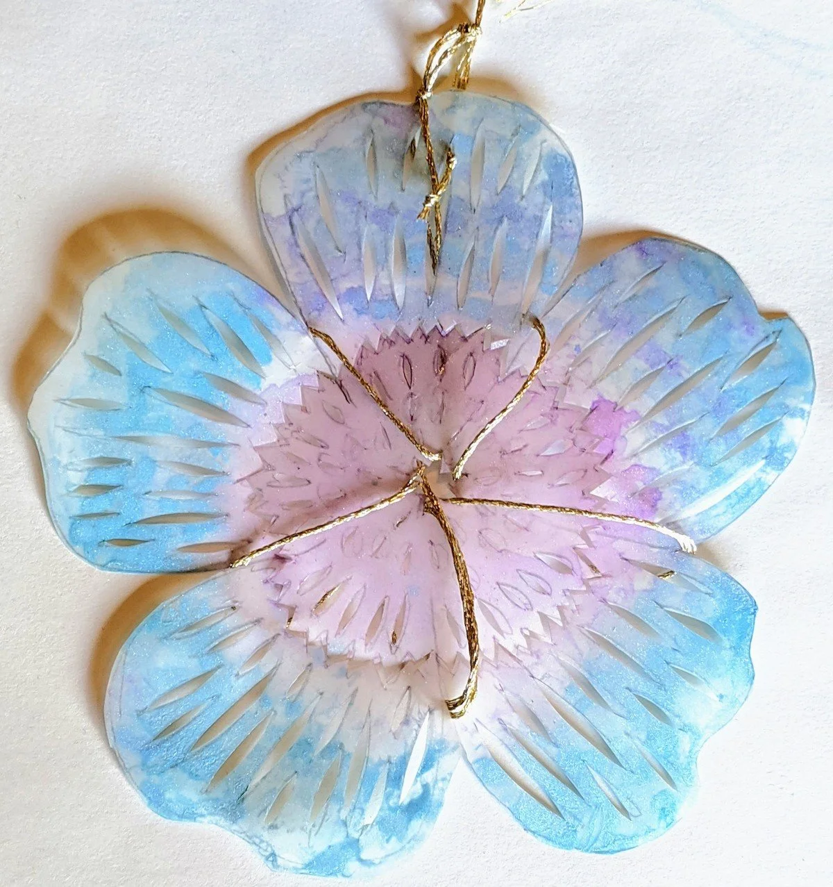 Colorful flower made of translucent paper, painted with gold accents, hanging from a gold string.