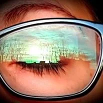 Close-up of a person's face wearing sunglasses with a reflection of a forest scene in the lenses.