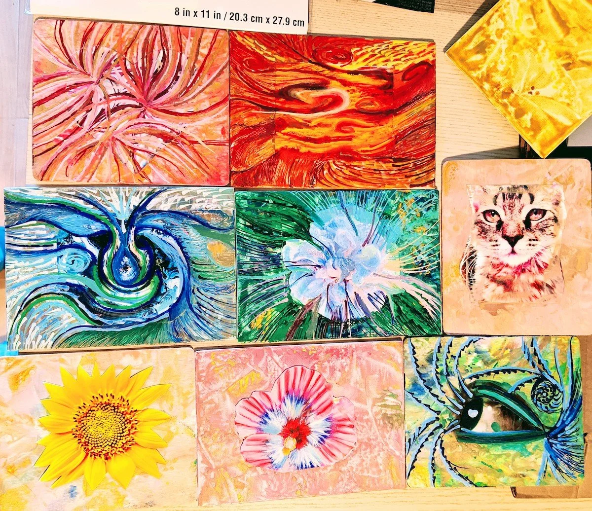 A collection of colorful artwork and paintings displayed on a wooden surface, including abstracts, a leopard photograph, and floral images.