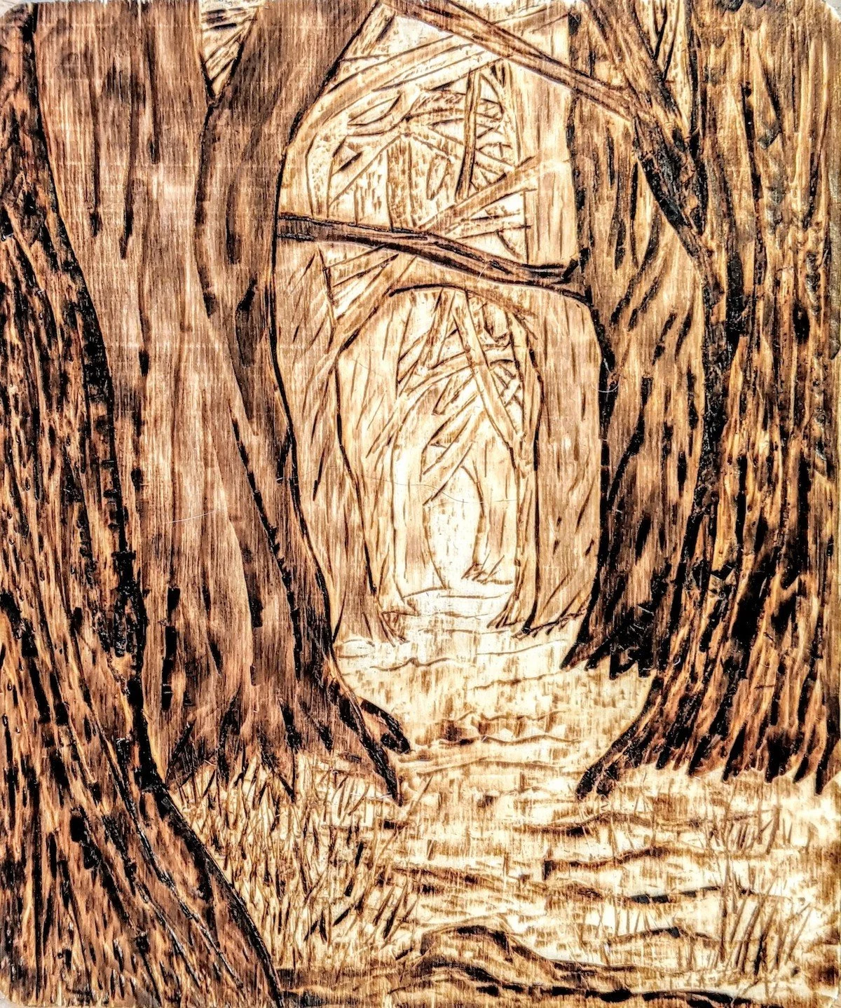 Wooden carving of a forest scene with trees and a pathway.