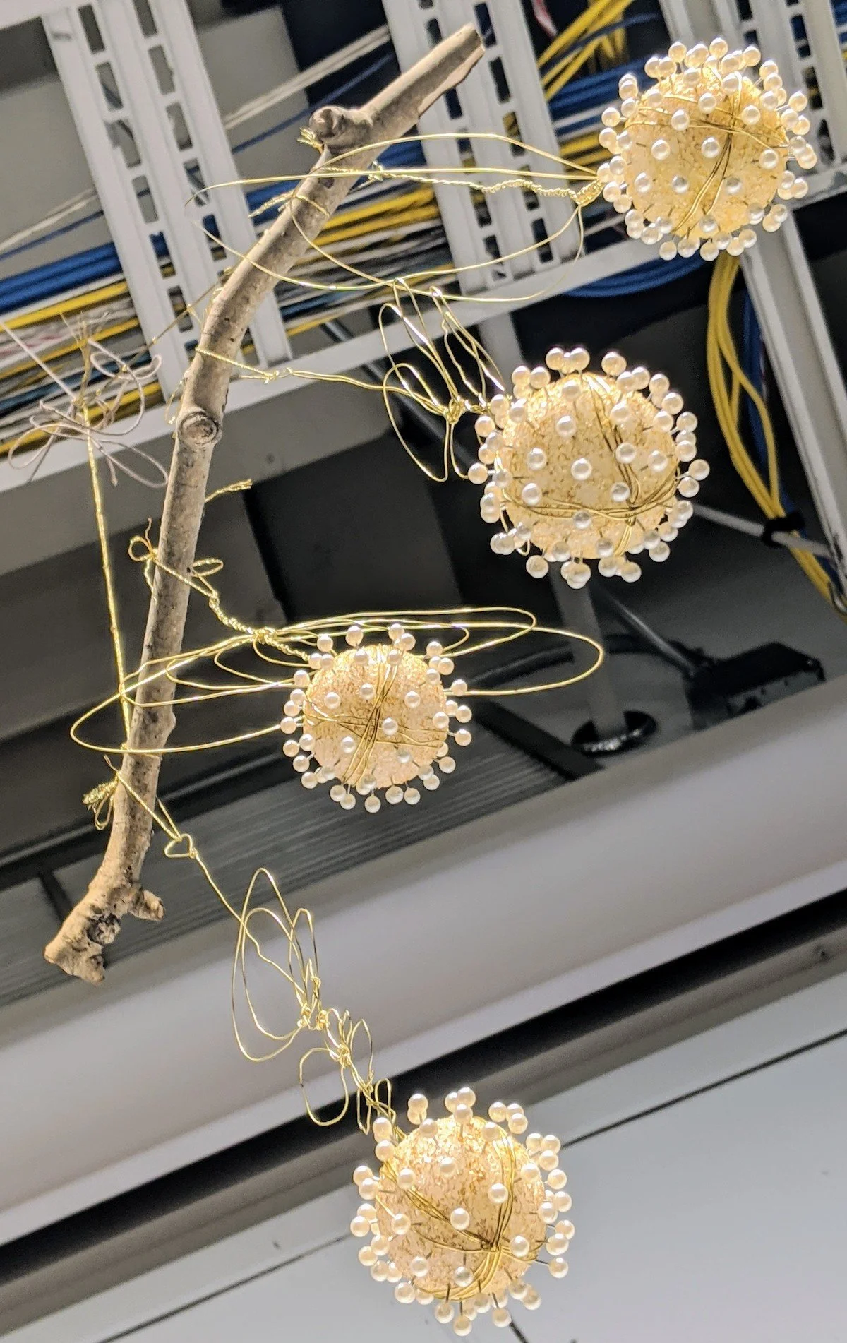 Decorative hanging art made of pearl-like beads attached to gold wire, suspended from a branch.