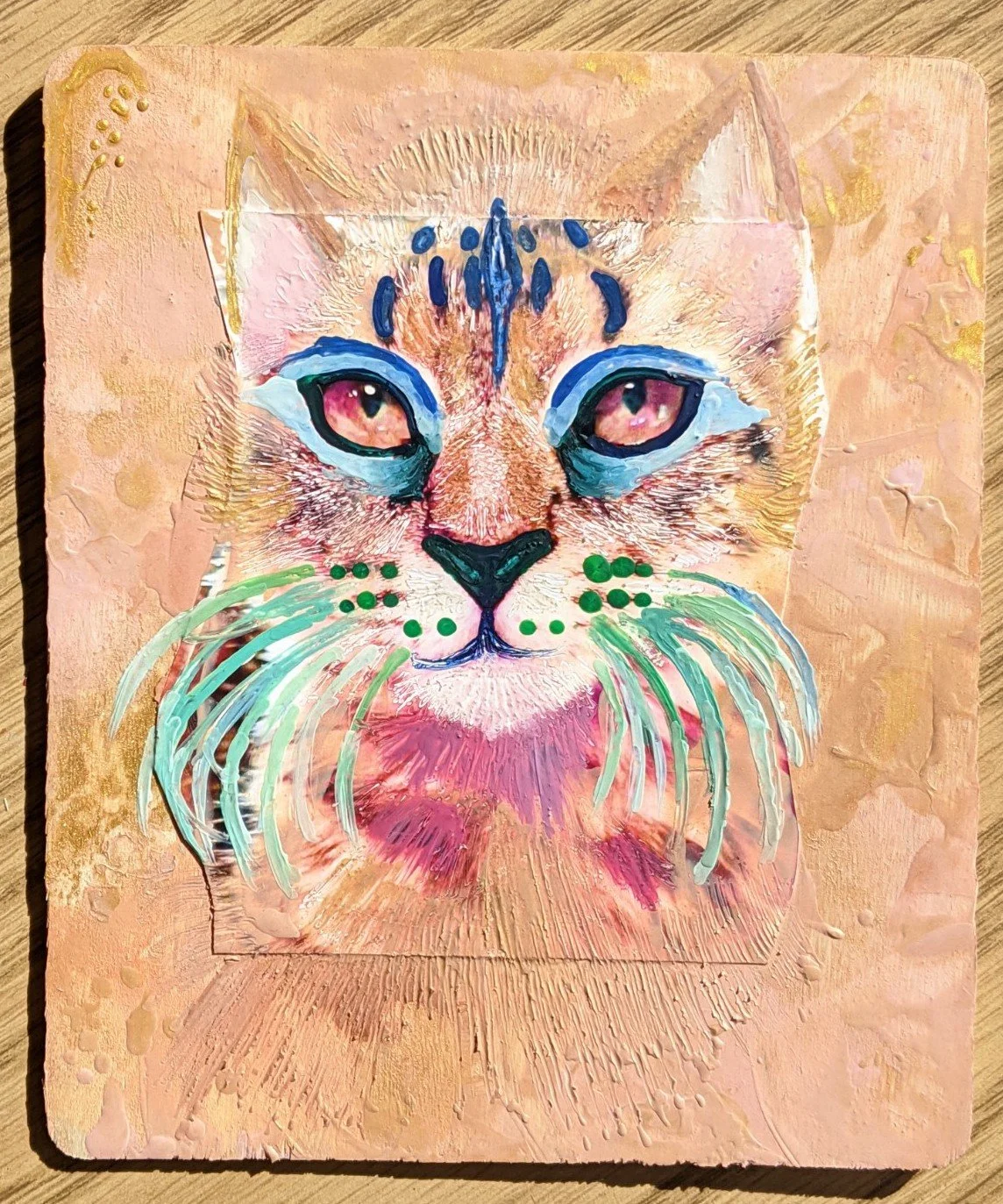 A mixed media portrait of a cat with pink eyes, featuring colorful accents including blue, green, and pink, on a textured peach background.