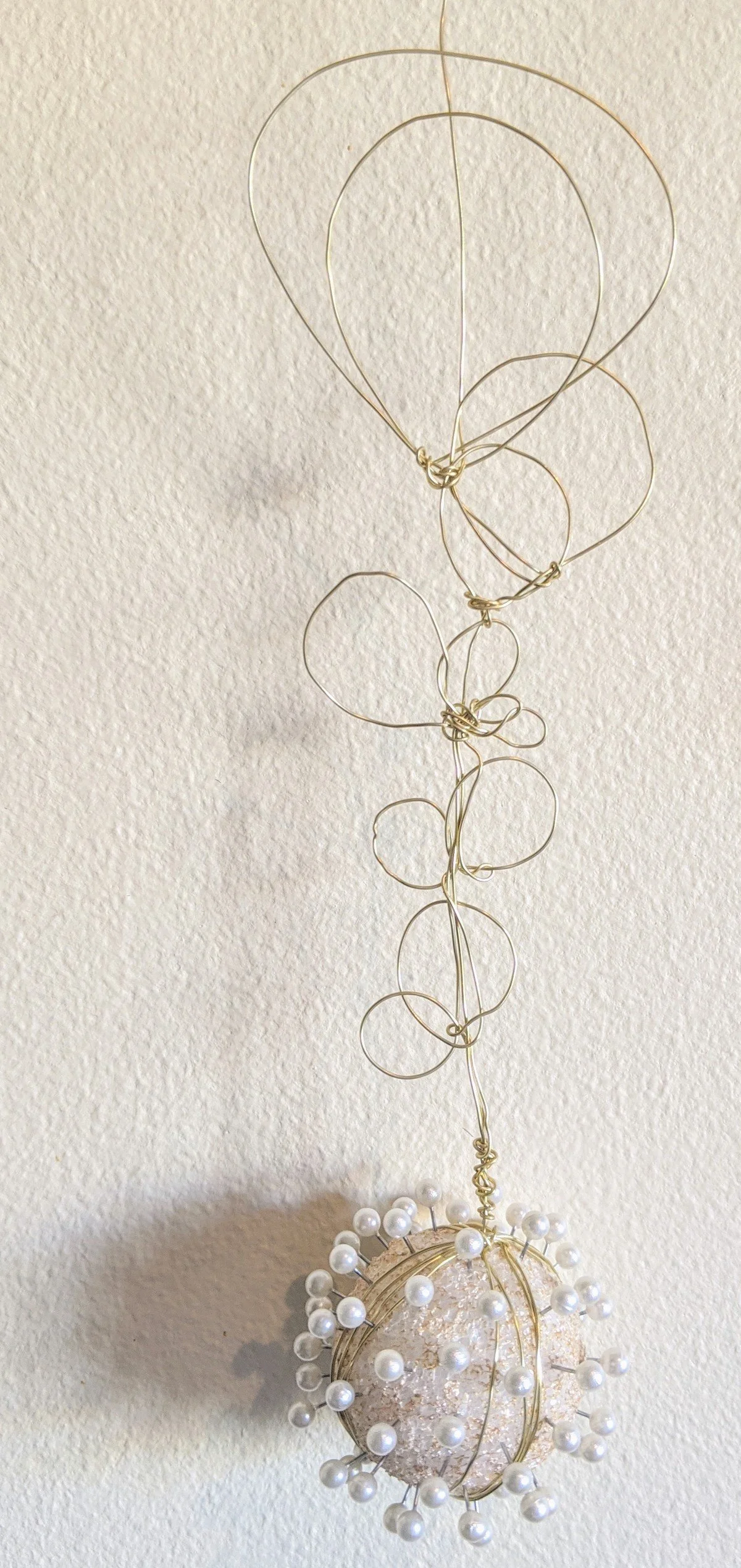 Decorative hanging ornament with a glass ball covered in pearls and wire spirals extending upward.