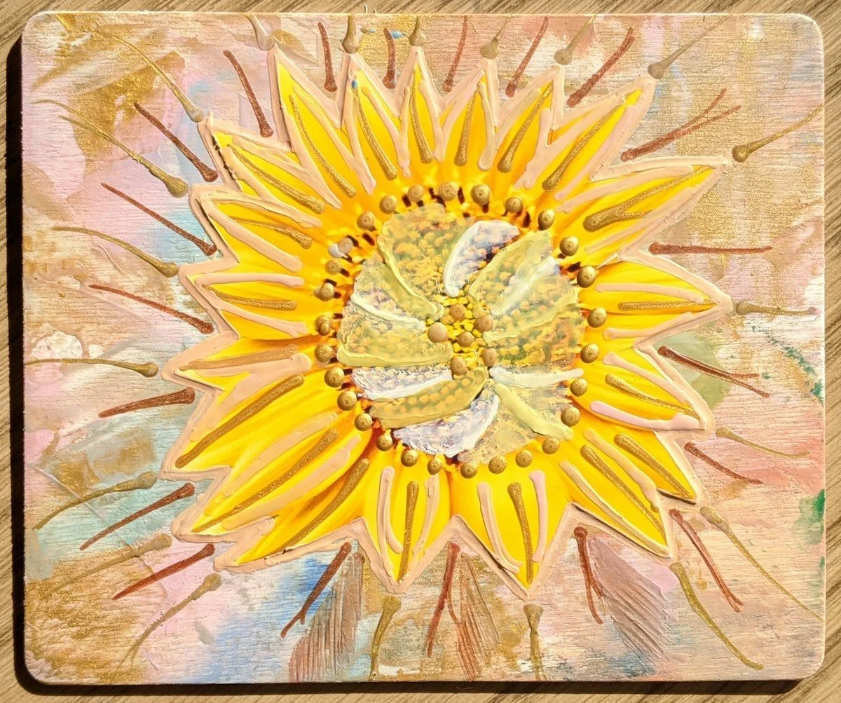 A sunflower-shaped dessert decorated with yellow, pink, and brown icing and small edible pearls, on a wooden surface.