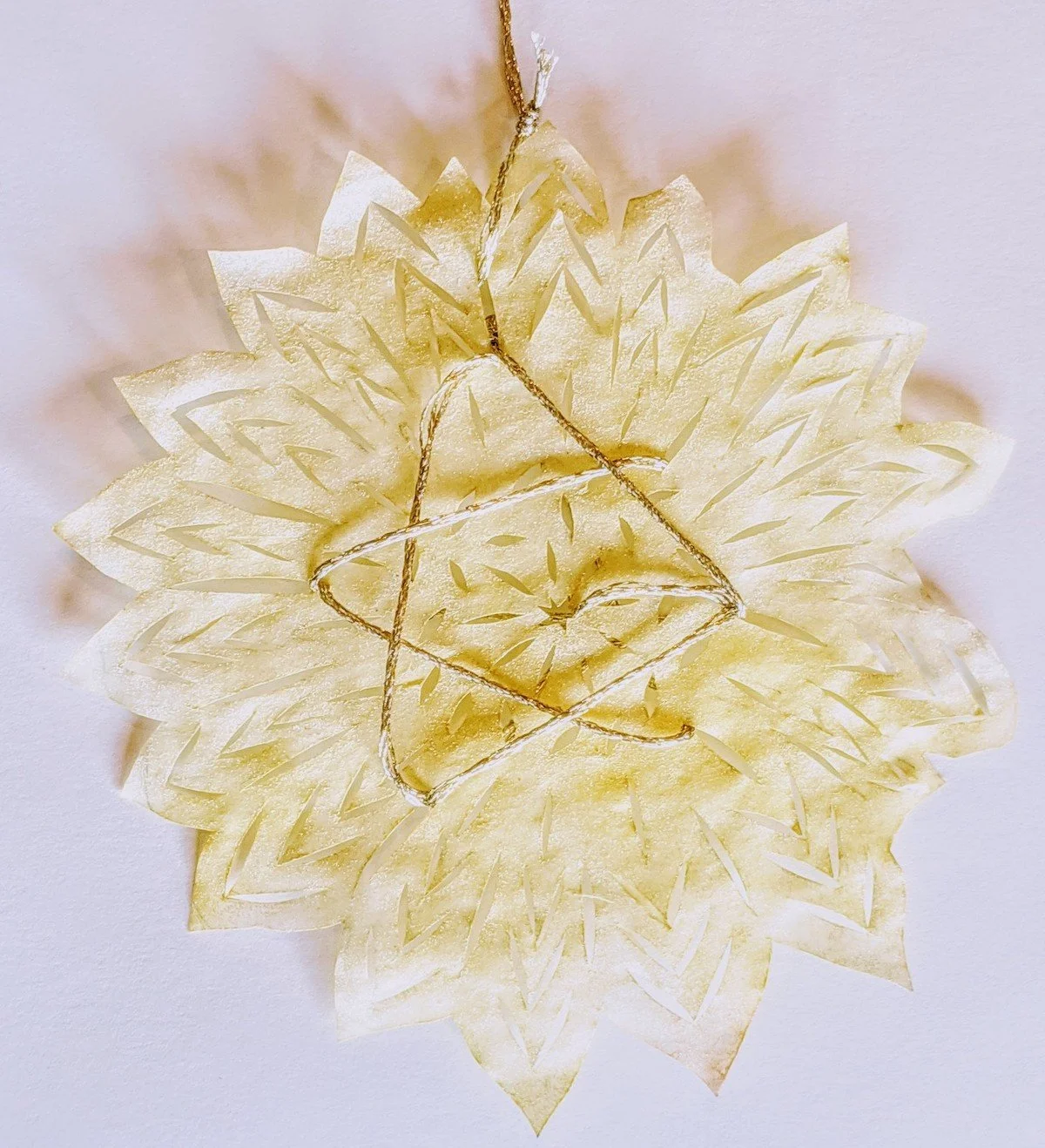 Cream-colored decorative flowery7kl6, with gold accents and a hanging gold string, set against a white background.