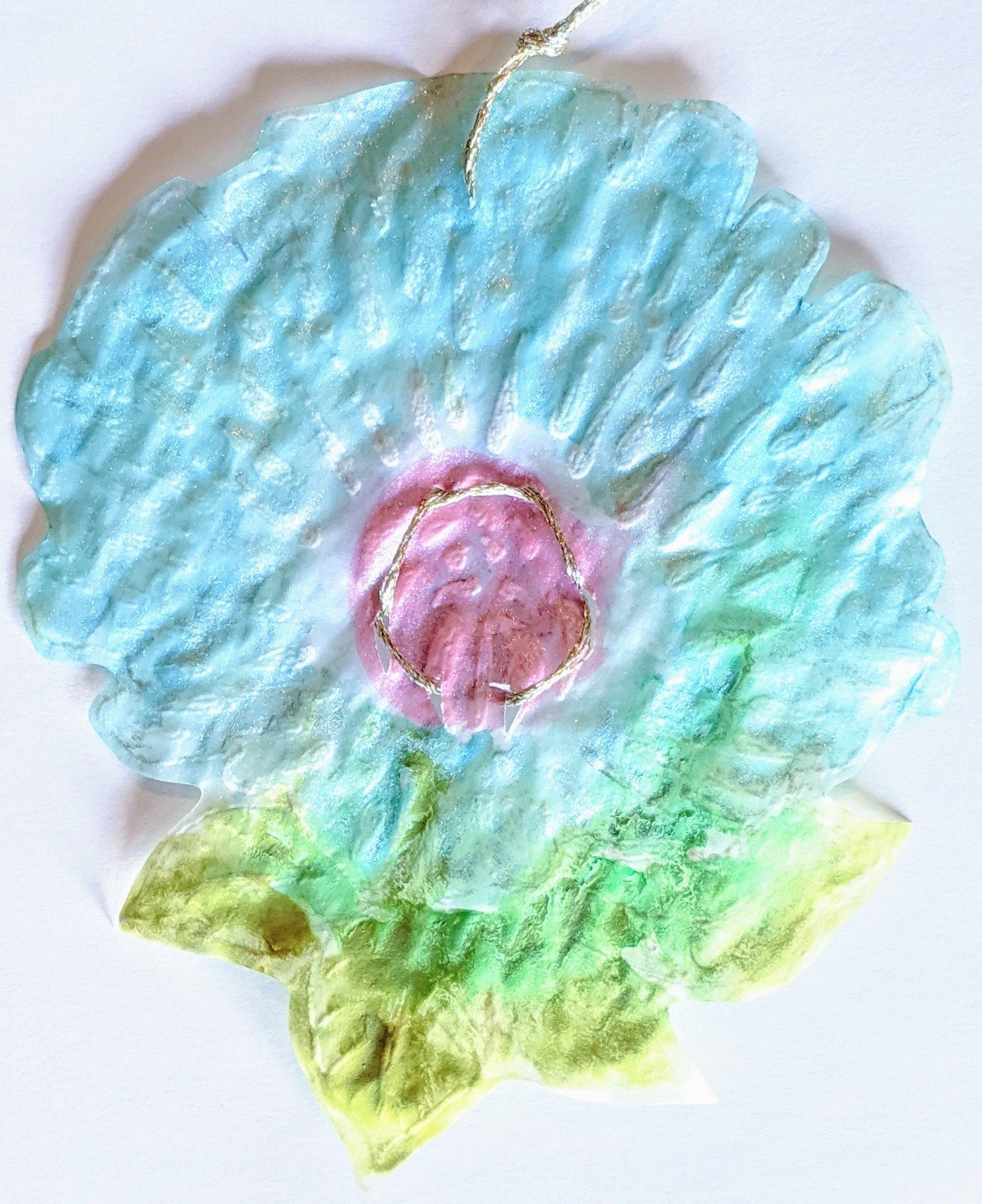 Colorful paper craft resembling a flower with pink, blue, and green hues, and gold accents.
