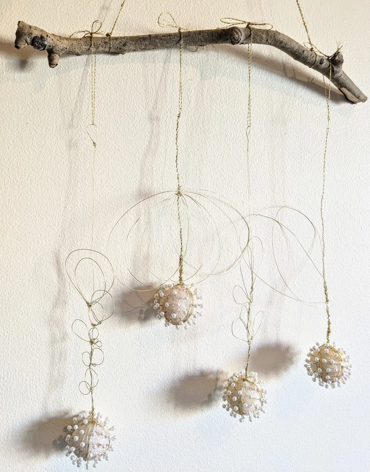Decorative hanging ornaments made of wire and pearl-like beads, suspended from a branch.
