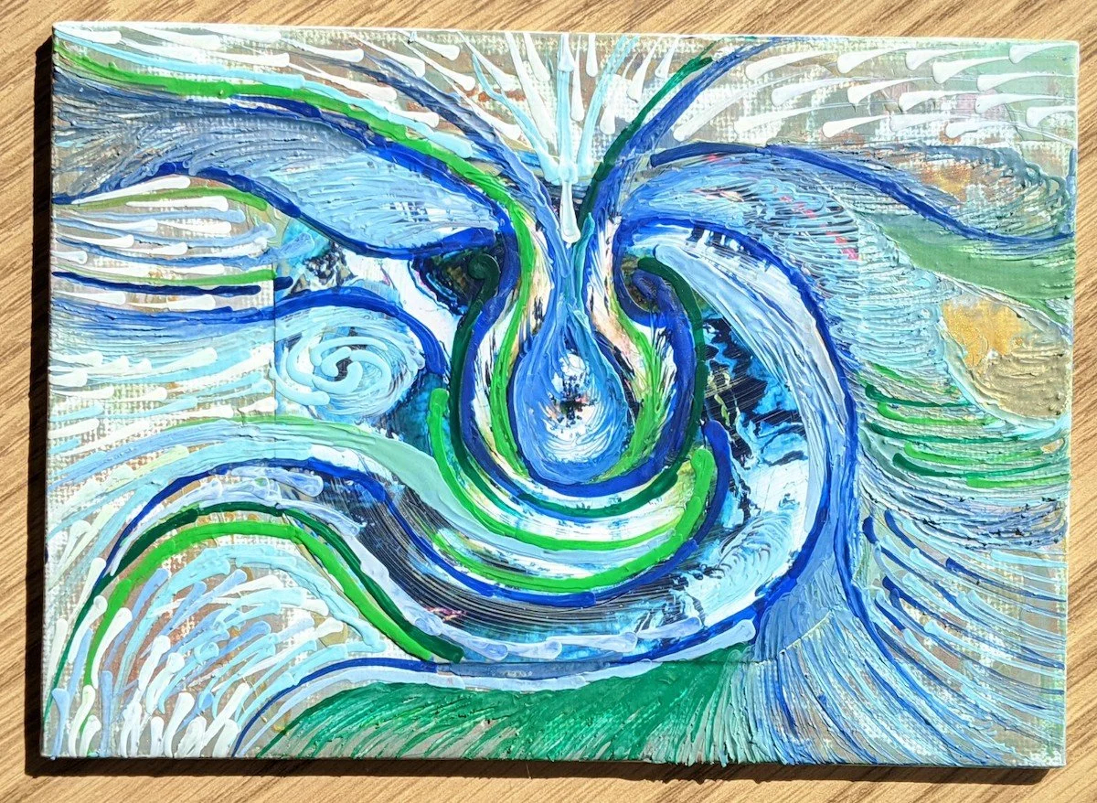 Abstract painting with swirling blue, green, white, and gold colors creating a vortex pattern on a canvas placed on a wooden surface.