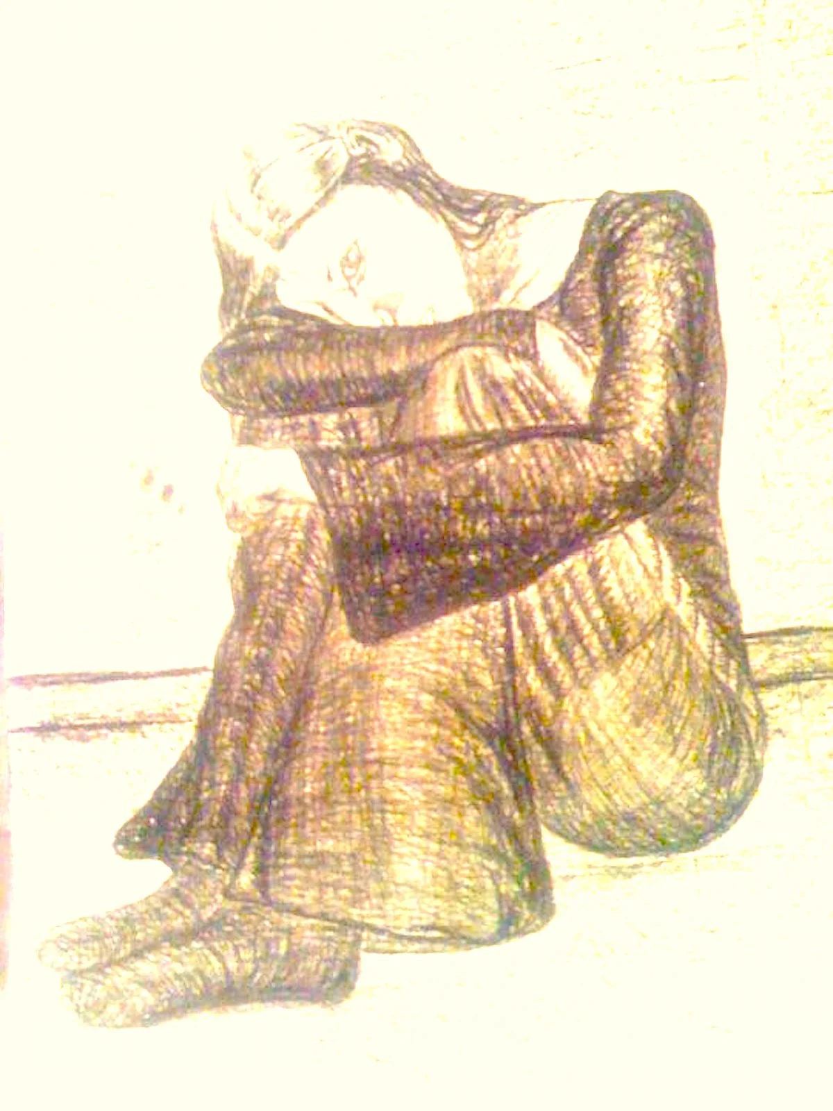 A woman is sitting on the floor with her knees bent and arms wrapped around her knees, resting her head on her forearms. She has long hair and is wearing a long-sleeved top and a skirt.