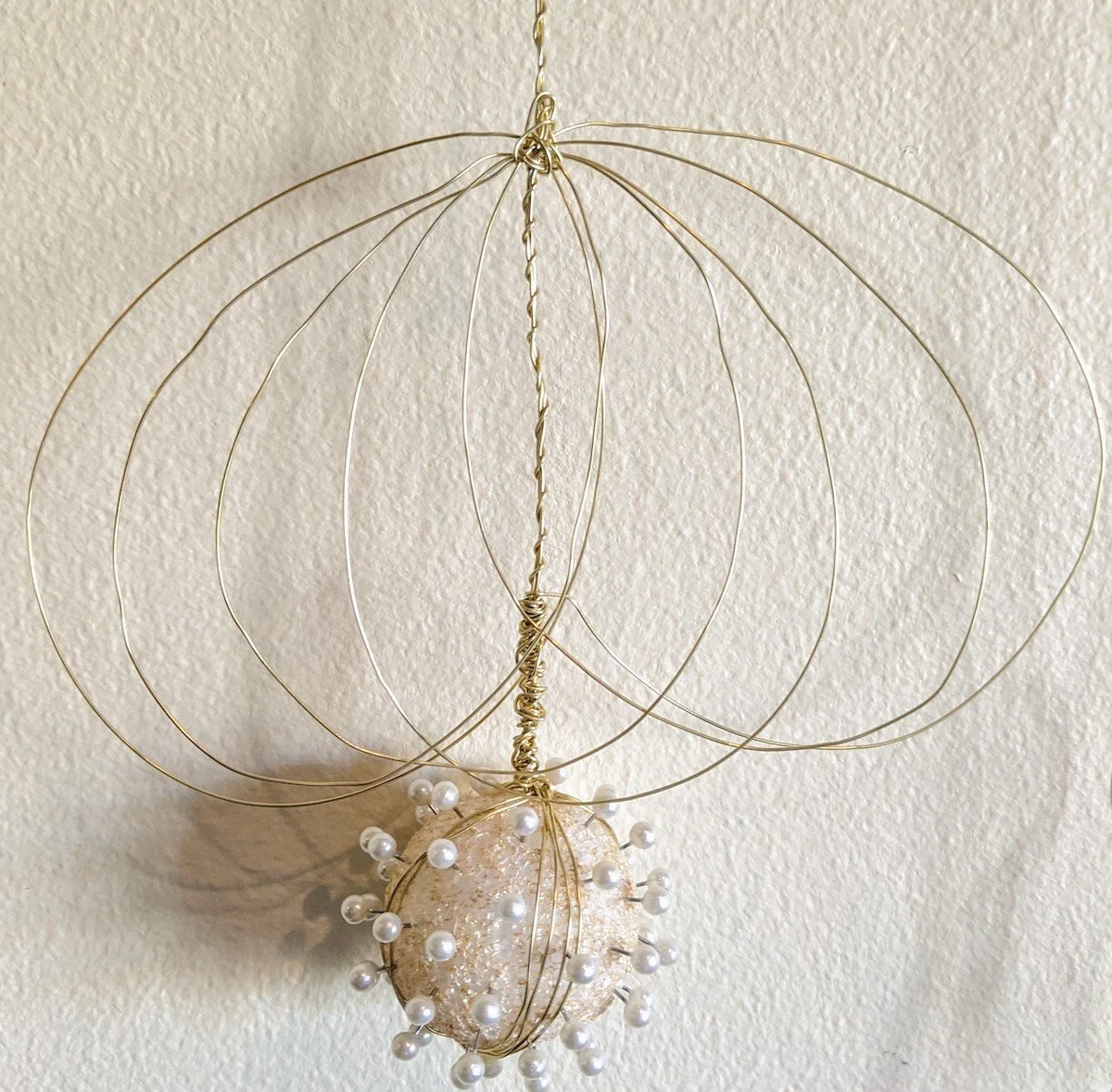 Decorative hanging ornament with thin gold wires forming a spherical shape. The bottom of the ornament features a pearl-beaded decorative element.