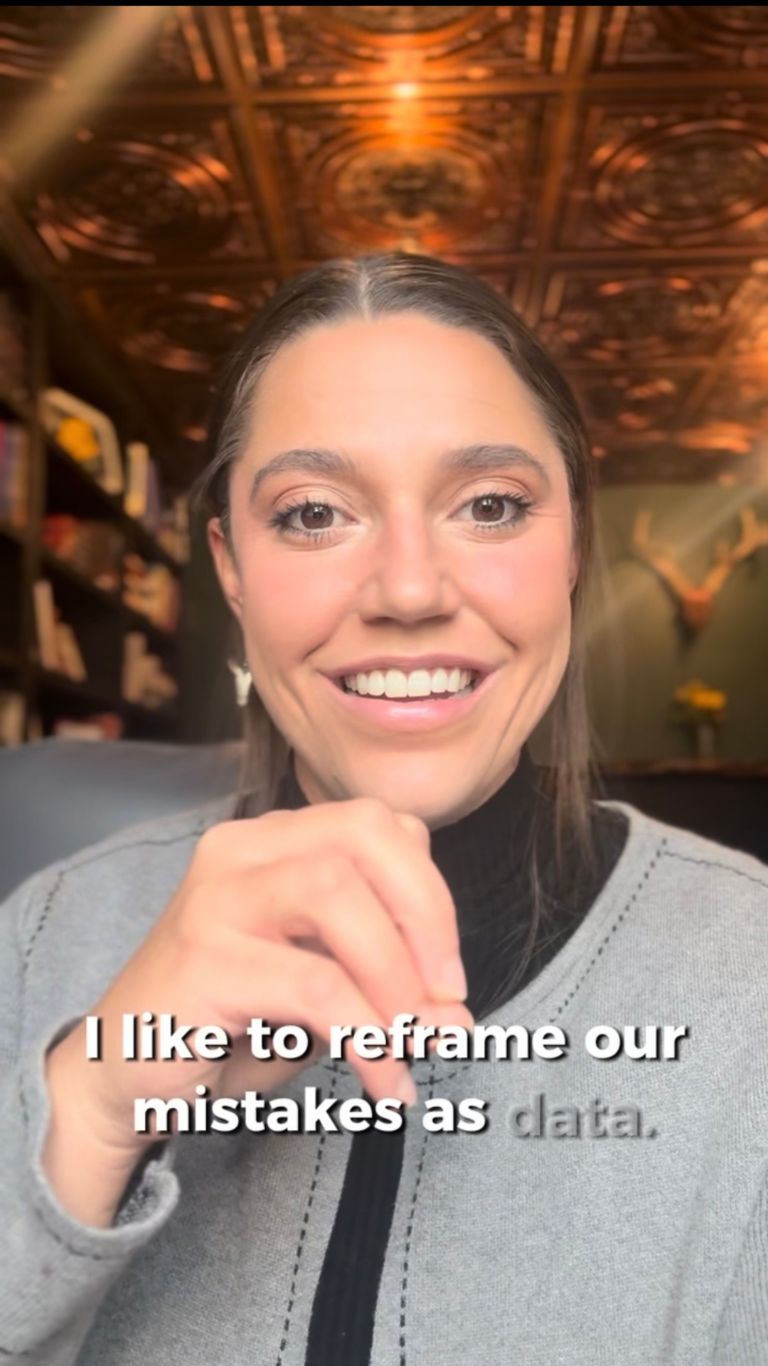 A woman with brown hair smiling at the camera inside a room with a decorative wooden ceiling and bookshelves in the background.