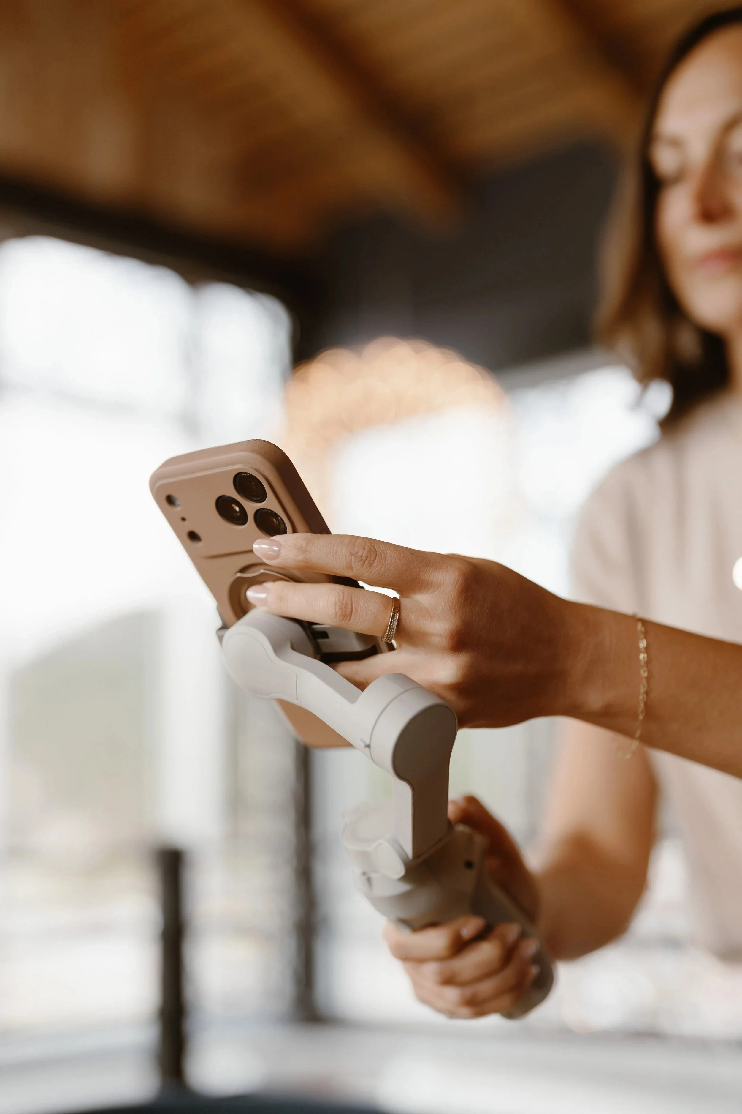 Close-up of a woman holding a smartphone attached to a stabilizer, with blurred background.