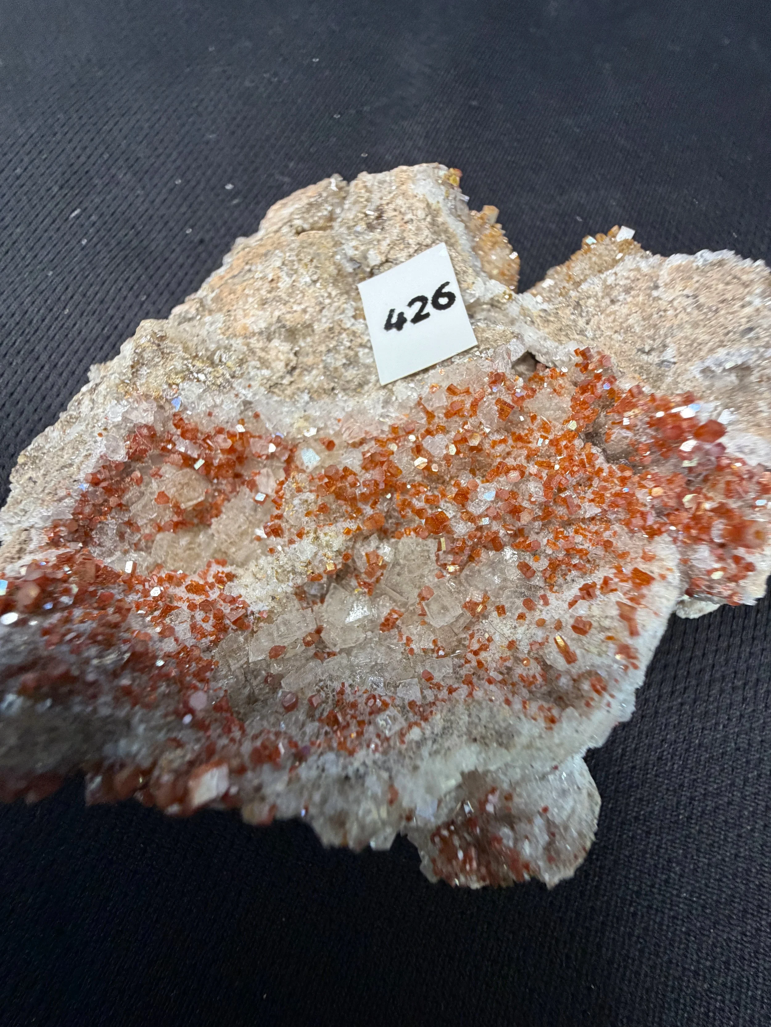 A vibrant and highly detailed vanadinite cluster featuring dense fields of sparkling hexagonal orange-red crystals scattered across a pale quartz and calcite matrix