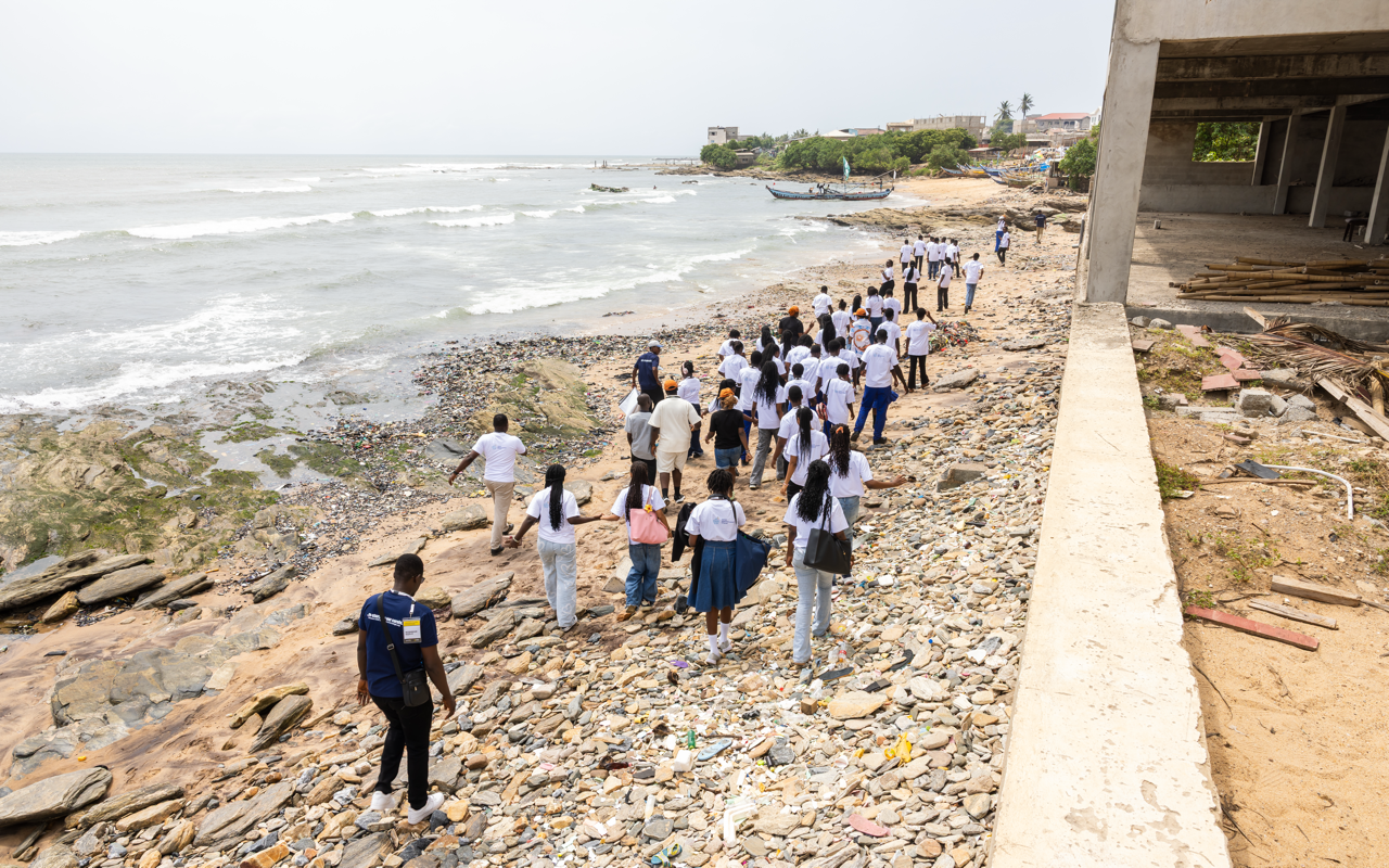 Group of people walking along a rocky beach near a partially constructed building.