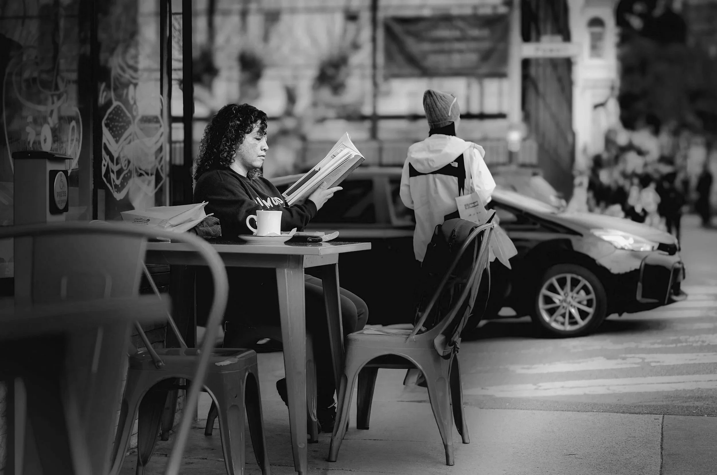 Black and white street photo of a woman reading outside a cafe in San Francisco.