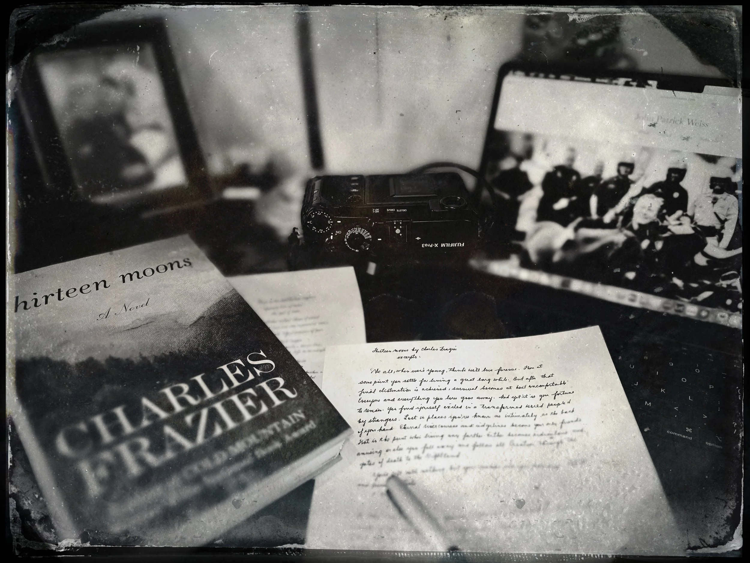 Black and white vintage style photo of Charles Frazier's novel "Thirteen Moons" beside handwritten notes, a rangefinder camera, and an open laptop.