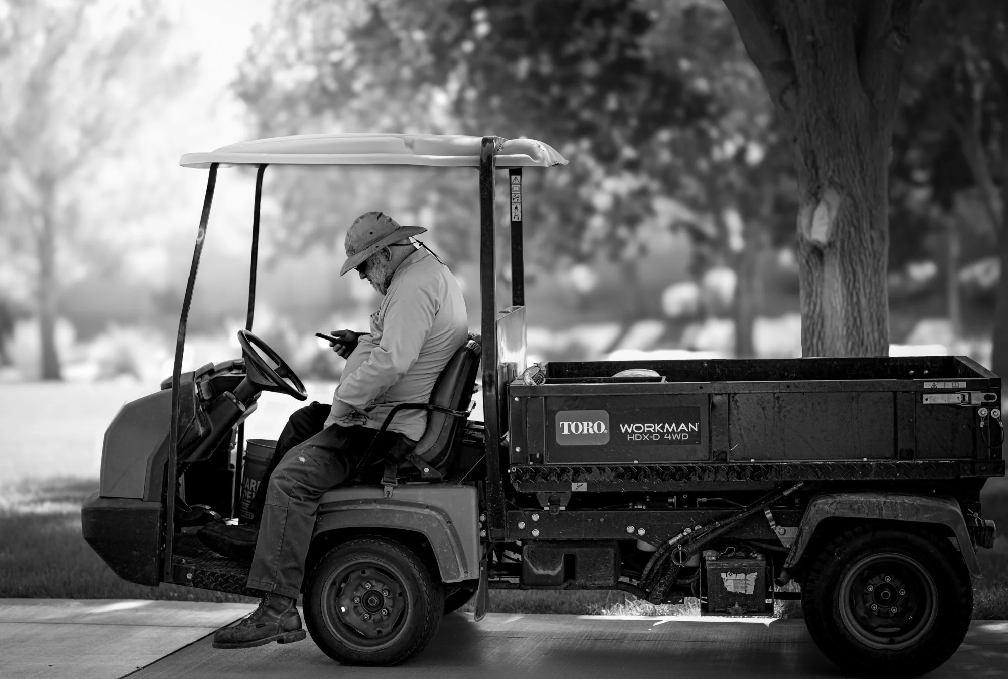 Black and white photo of groundskeeper seated in a Toro Workman utility vehicle.