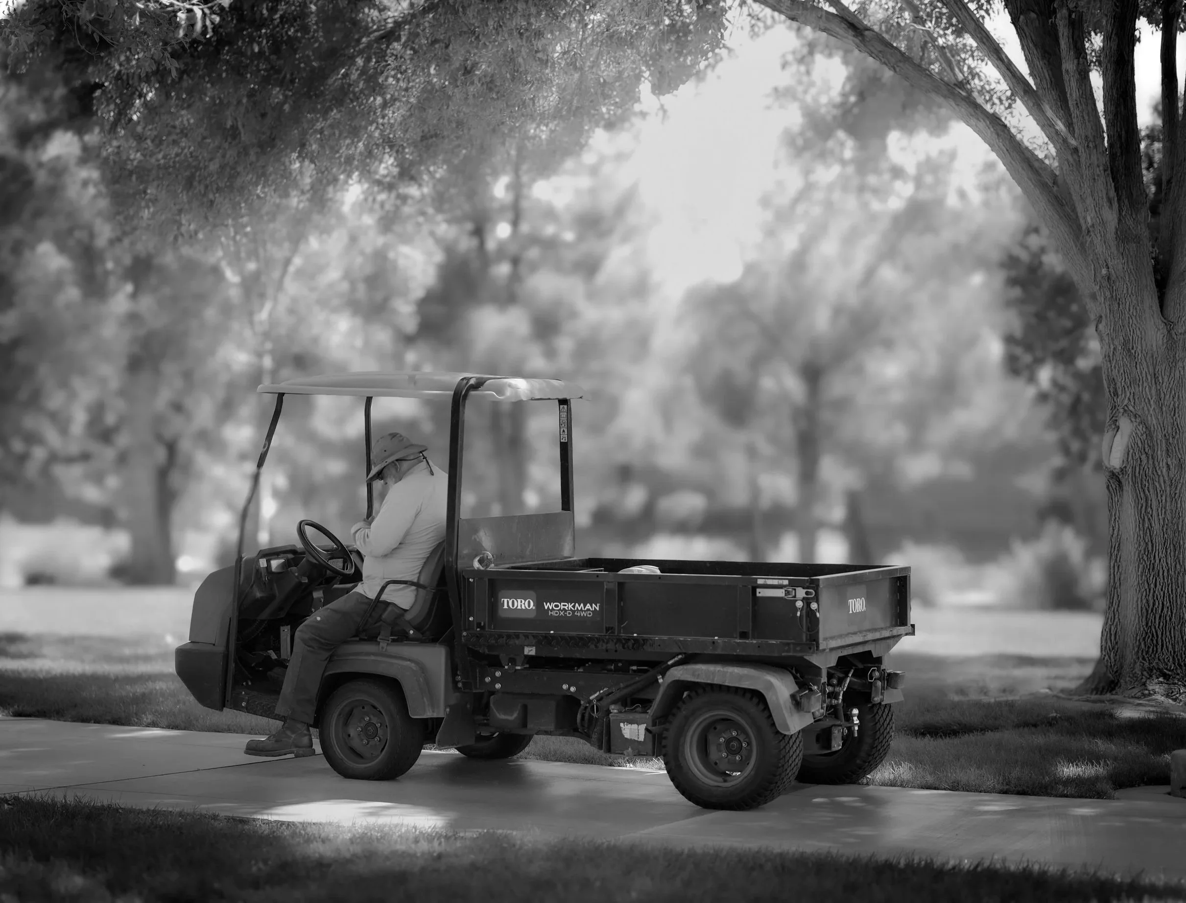 Black and white photo of groundskeeper seated in a Toro Workman utility vehicle.