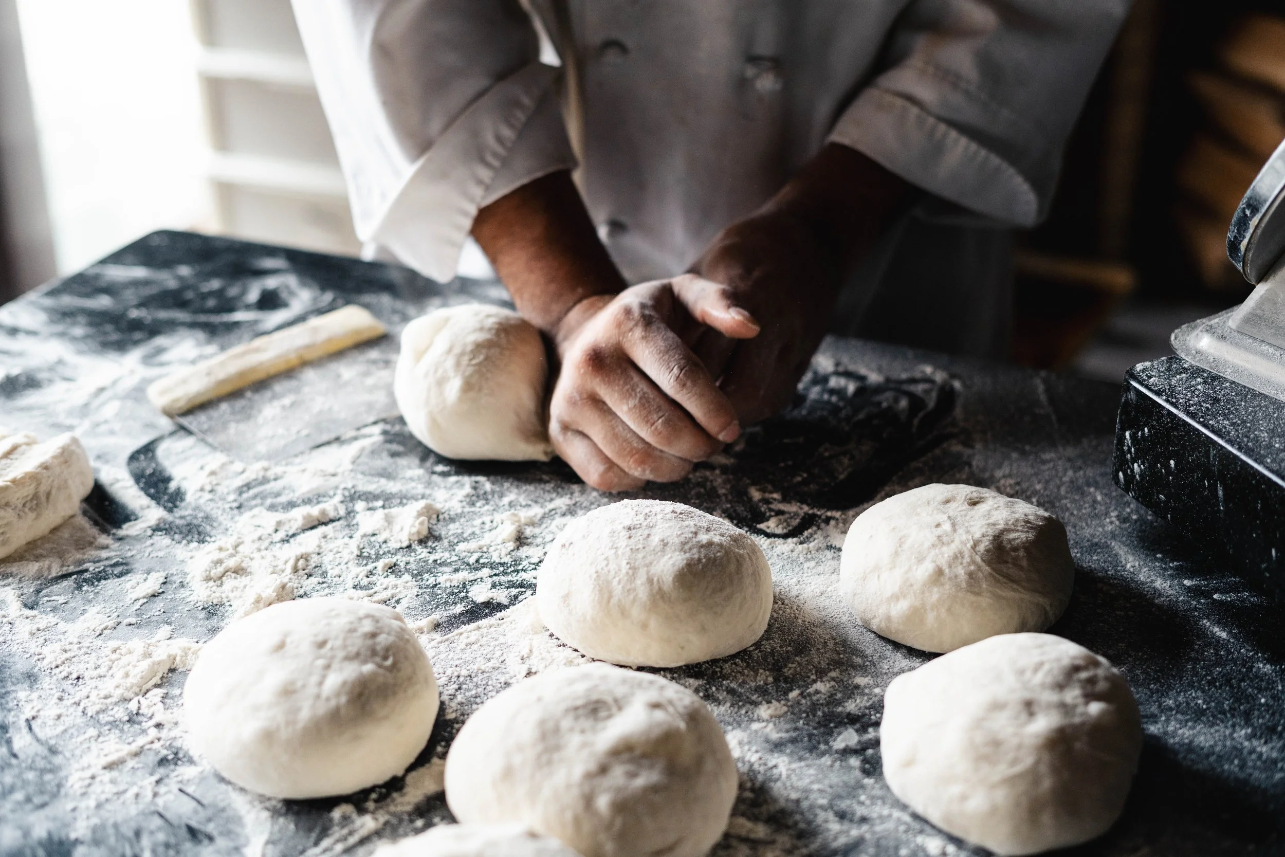 Person kneading dough on a floured countertop with multiple dough balls.