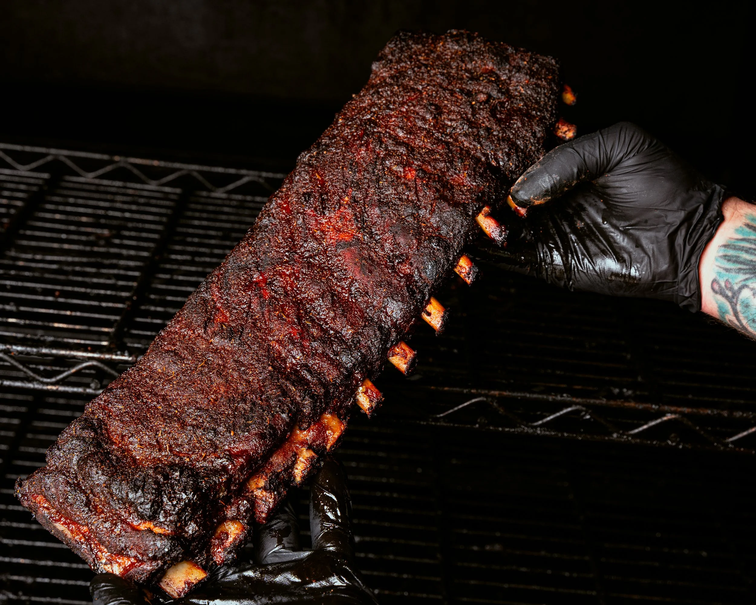 Person in black gloves holding a smoked rack of barbecue ribs.