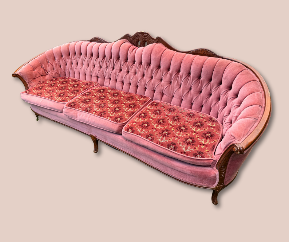 Vintage pink upholstered sofa with wooden frame and three floral-patterned cushions.