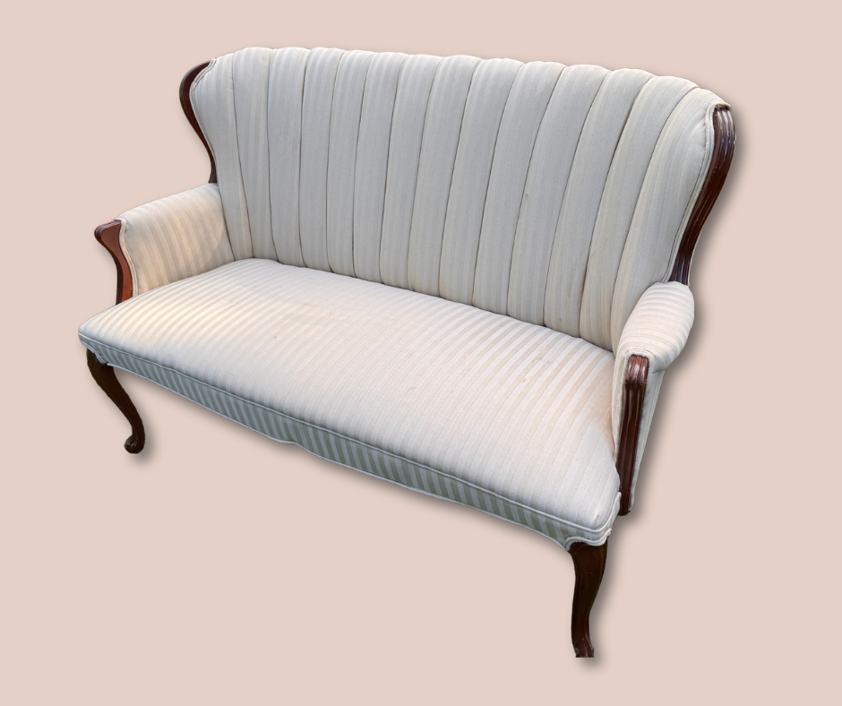 A vintage-style cream-colored sofa with vertical striped upholstery, wooden armrests, and carved wooden legs, placed on a plain beige background.
