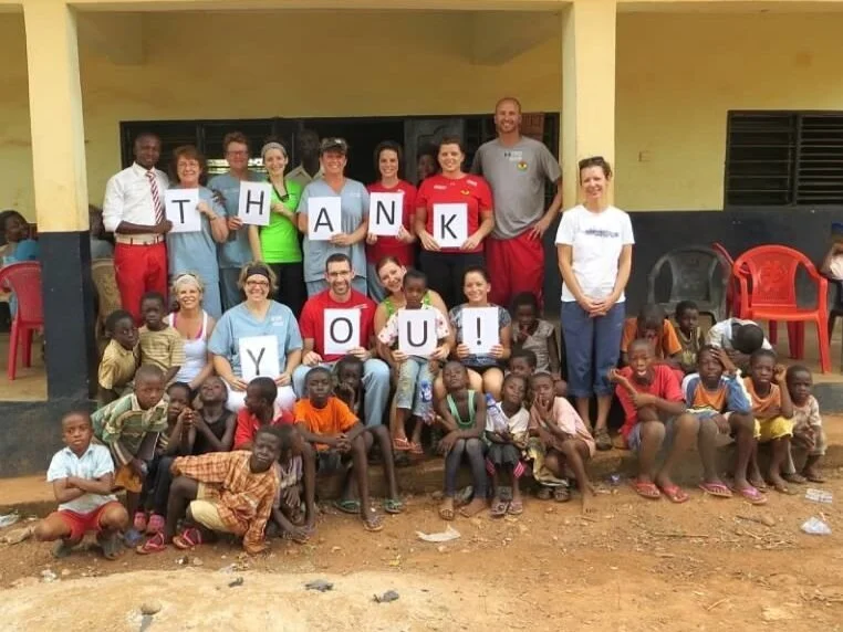 Group of children and adults outside a building holding signs that spell 'THANK YOU!'