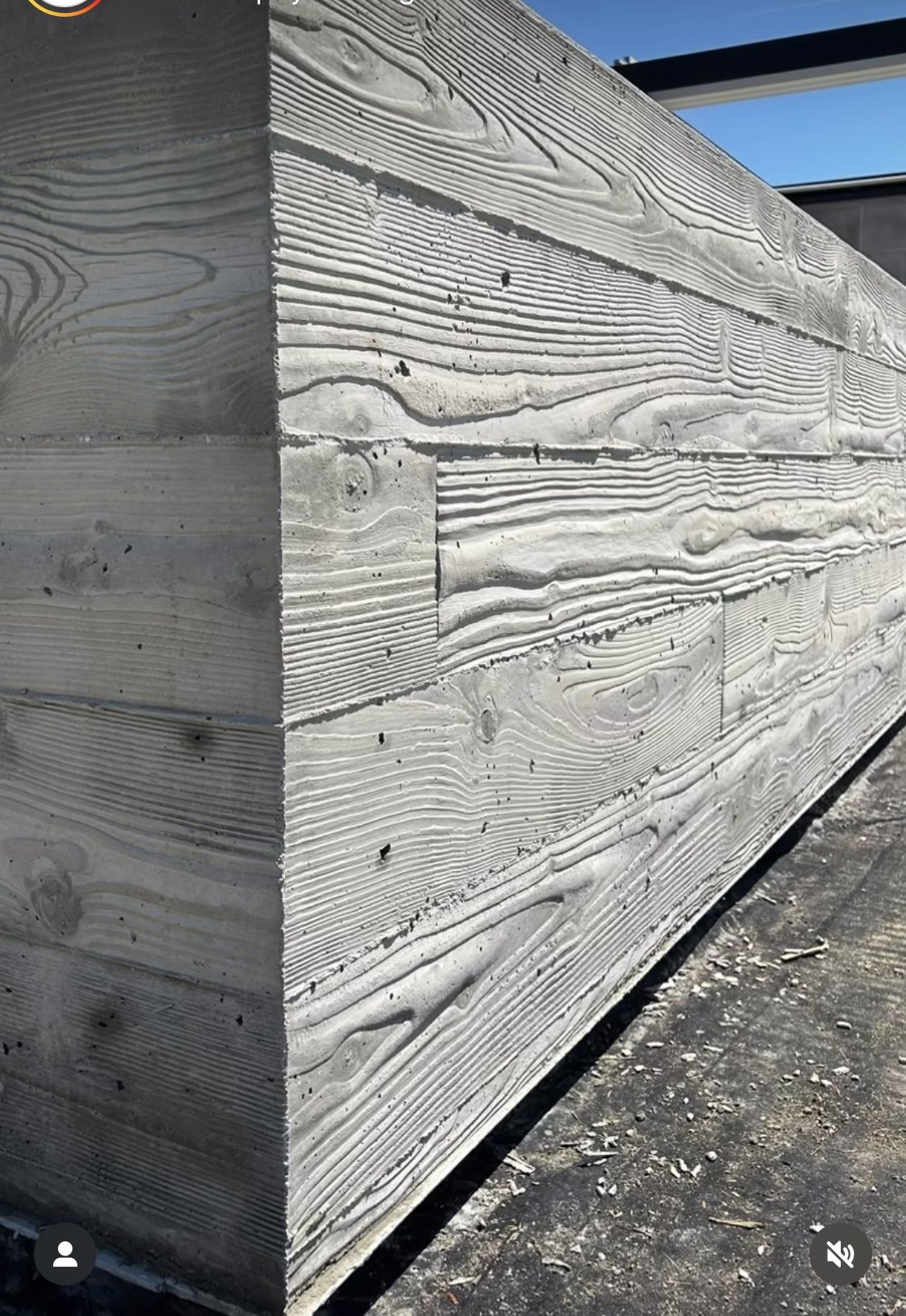 Close-up of stacked weathered wooden planks with visible grain patterns, cracks, and small black spots, outdoors against a clear blue sky.
