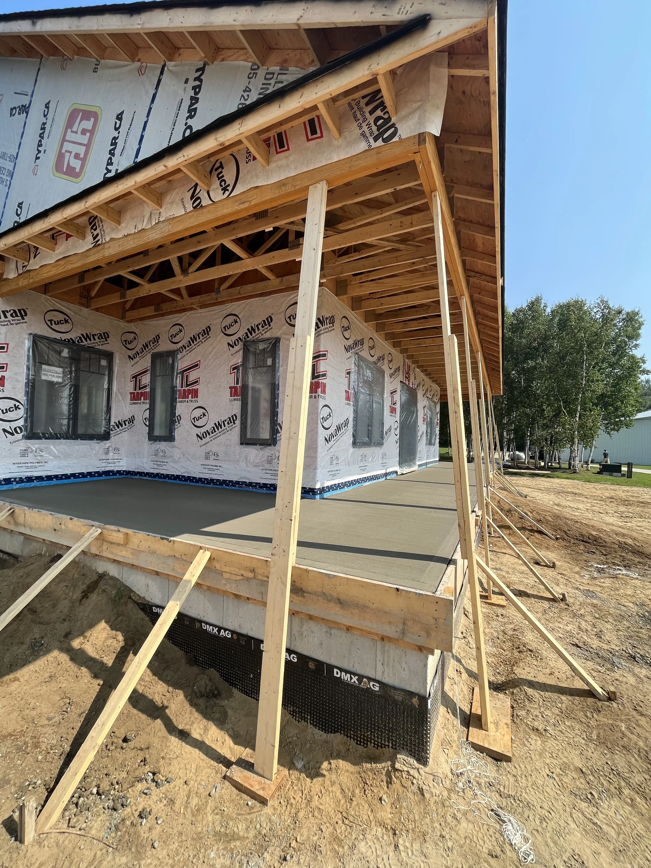 Construction site of a building with exposed wooden framing, wrapped in building materials, and some windows installed on the lower level.