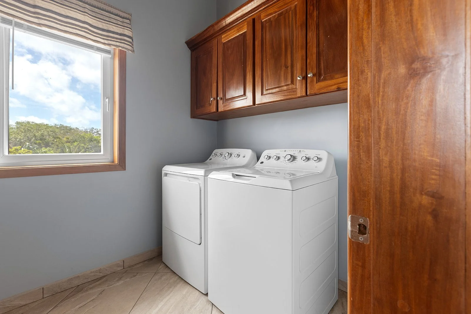 A laundry room with a window, cabinet storage, and a white washing machine and dryer.