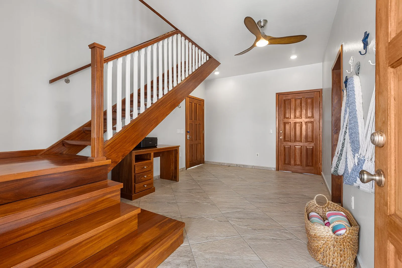 Living room with wooden staircase, tiled floor, wooden doors, ceiling fan, wall hooks with towels, and a basket of striped balls.