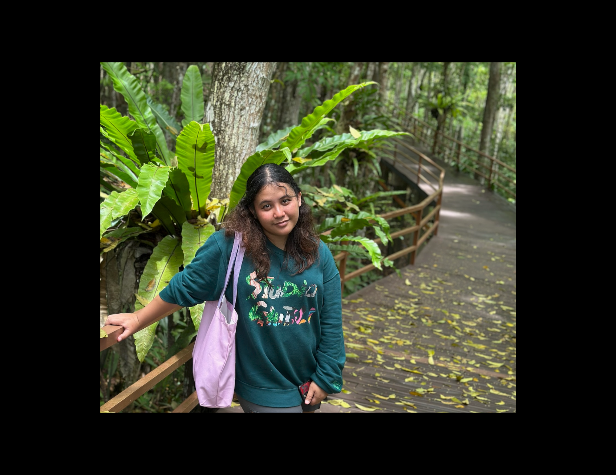 A young woman smiling outdoors surrounded by green plants.