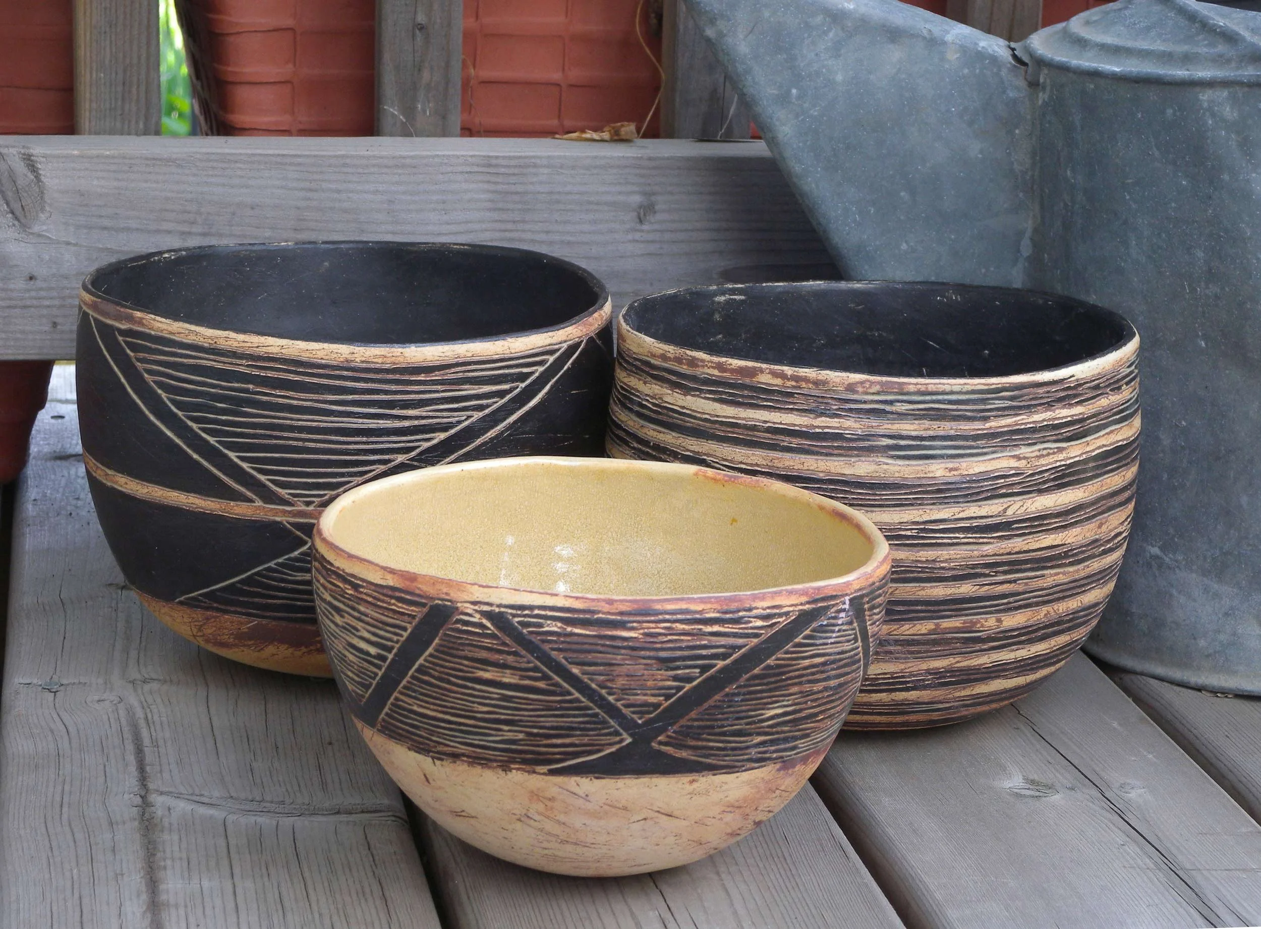 Stacked black and beige ceramic bowls with geometric patterns on a weathered wooden surface.
